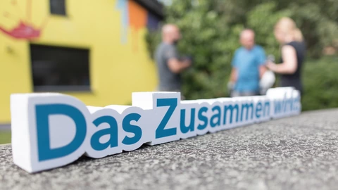Bild zeigt Slogan "Das Zusammen wirkt", im Hintergund sind Personen