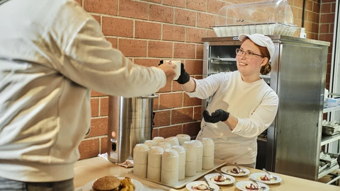 Auszubildende gibt Gast einen Kaffee in der Großküche im BBW Offenburg