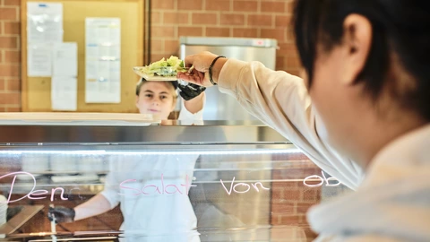 Auszubildende reicht Gast einen Salat an der Salattheke