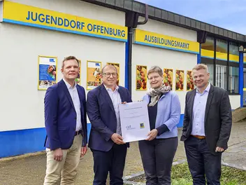 Vier Personen von EDEKA Südwest und CJD vor dem Ausbildungsmarkt bei der Unterzeichnung der Kooperationsvereinbarung.