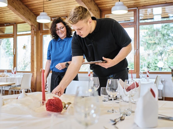 Auszubildender deckt in Begleitung der Ausbilderin den Tisch im Ausbildungsrestaurant Sägeteich im CJD BBW Offenburg