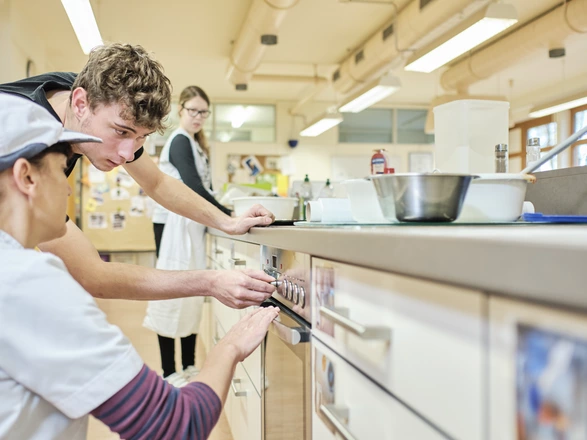 Zwei Personen stellen die Spülmaschine in der Ausbildungsküche im CJD BBW Offenburg ein, eine weiter Person ist im Hintergrund
