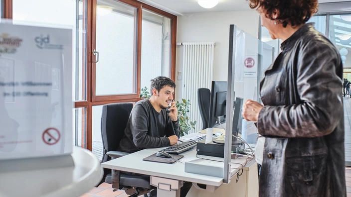 Auszubildender am Schreibtisch telefoniert, im Vordergund die Ausbilderin